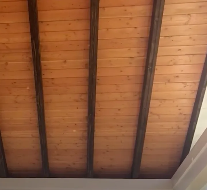A timber-lined ceiling with pale tongue-and-groove boards running between dark-stained exposed timber beams